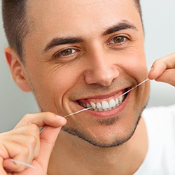 Man with dental implants in Reynoldsburg flossing and smiling