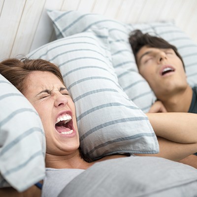 man snoring and woman covering ears and screaming